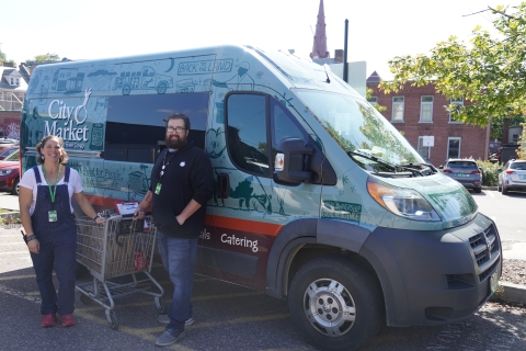 Our newly wrapped in fun 50th anniversary branding delivery van is parked. Max and Val, the delivery team, are smiling while posing with a shopping cart in front. 