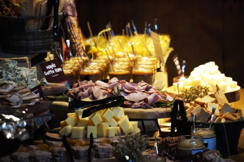 Many platters of food are arranged artfully on a table. There are cubes of cheese, folded slices of cotto ham, artisan mustard, pots de creme, and more.