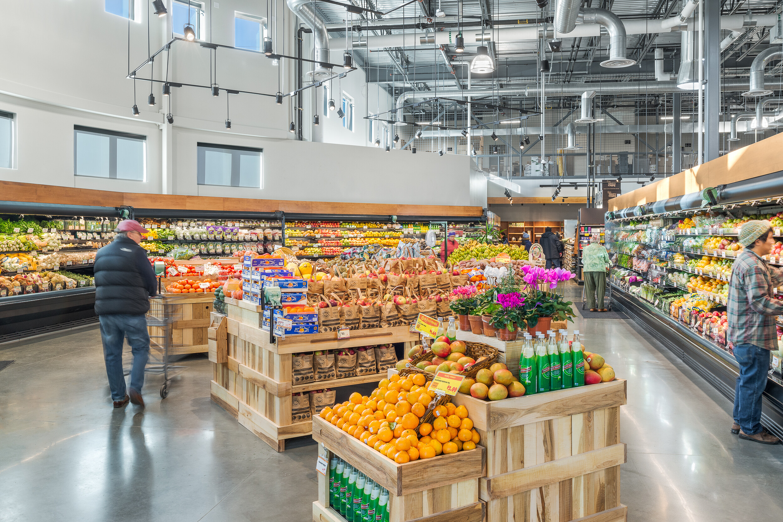Bright grocery store interior filled with various fruits, vegetables, and shoppers.