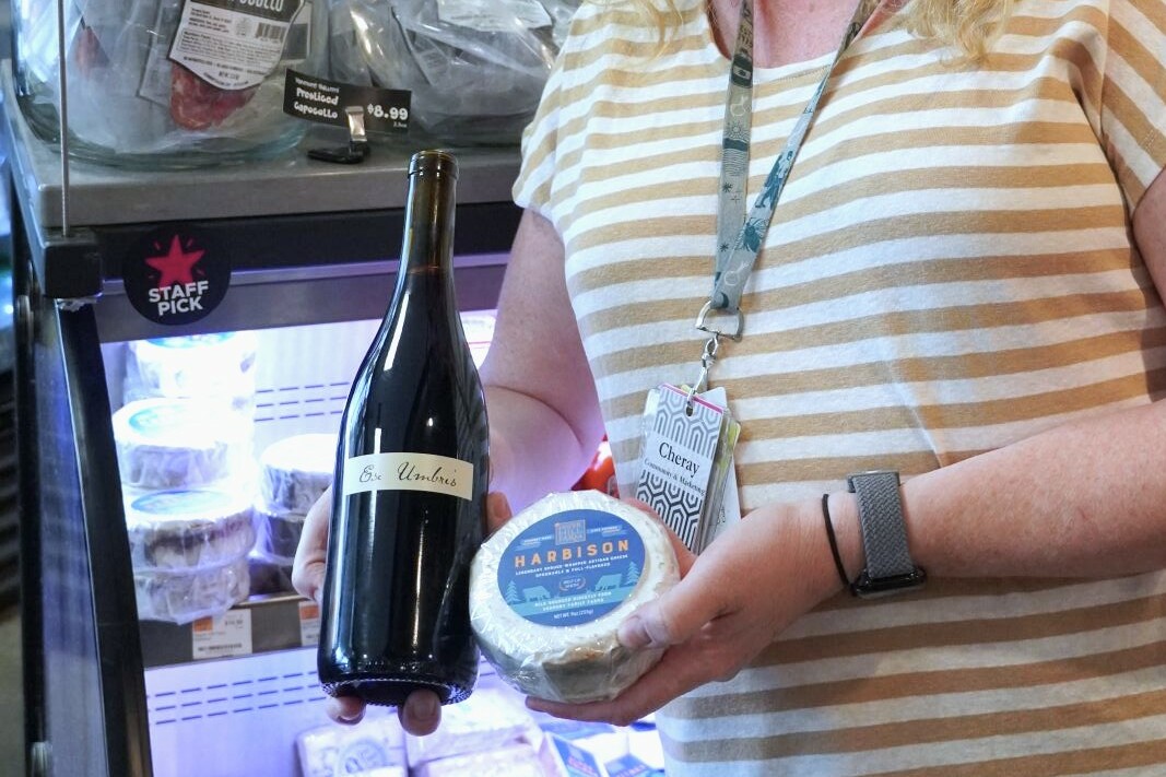 A woman holds up a bottle of wine and cheese block