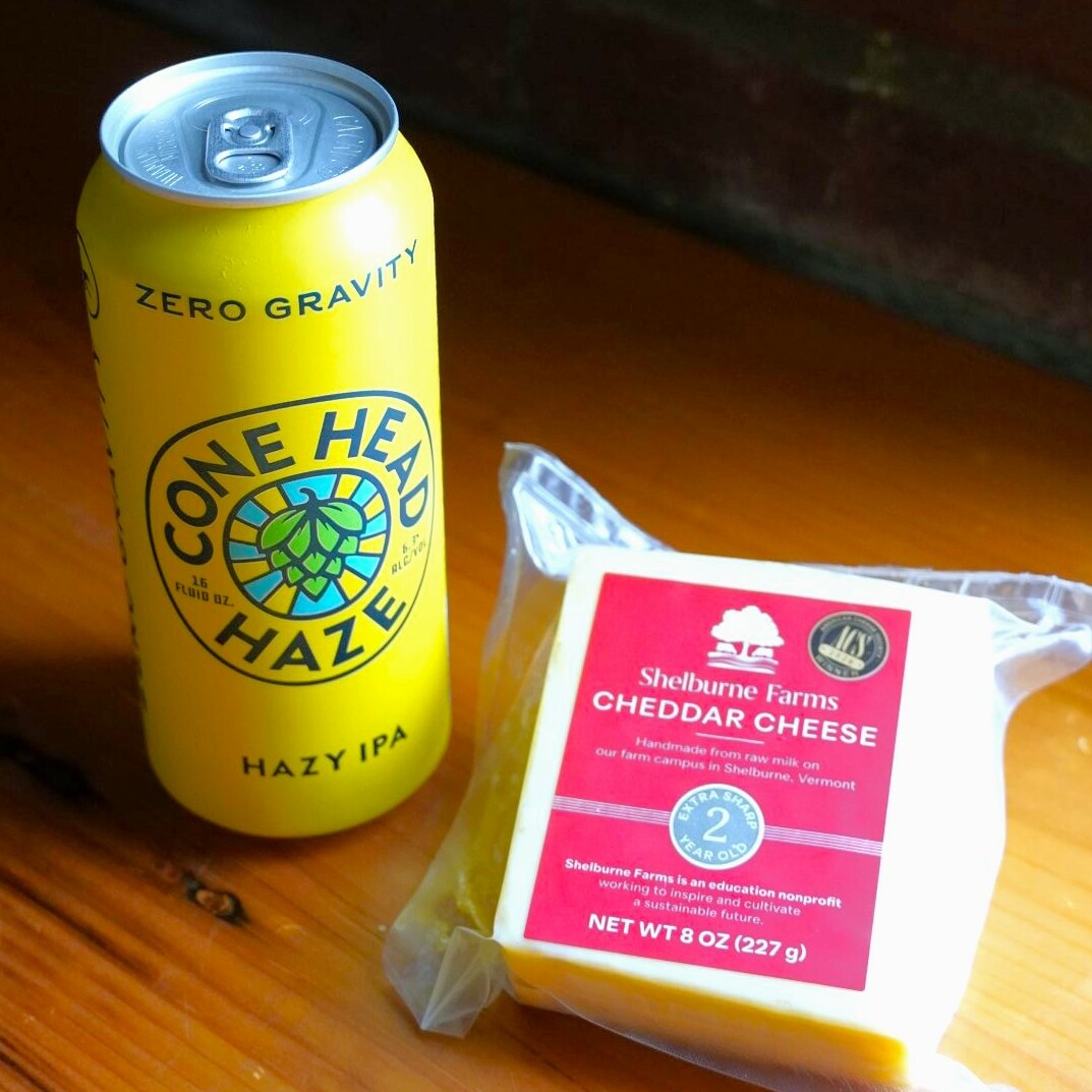 A can of Cone Head Haze IPA next to Shelburne Farms cheddar cheese.