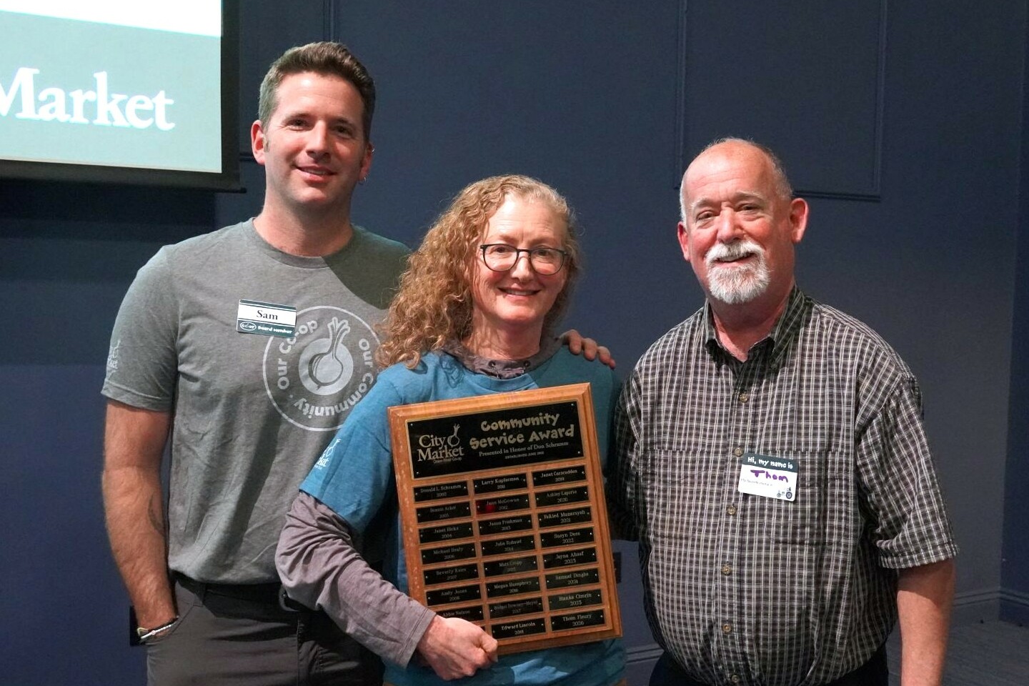 3 people stand one with an award in hand