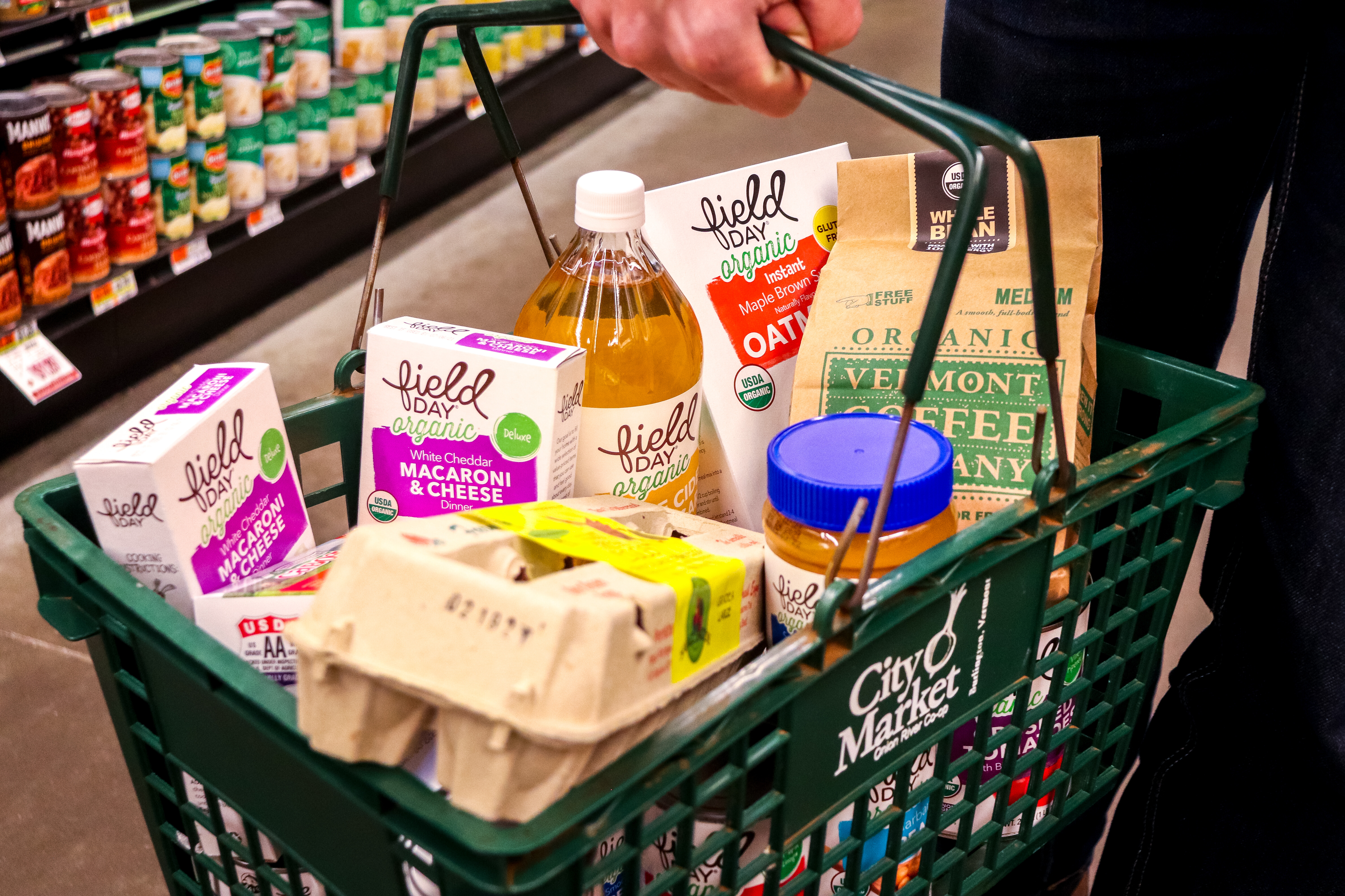 A green shopping basket filled with organic food items at a grocery store.