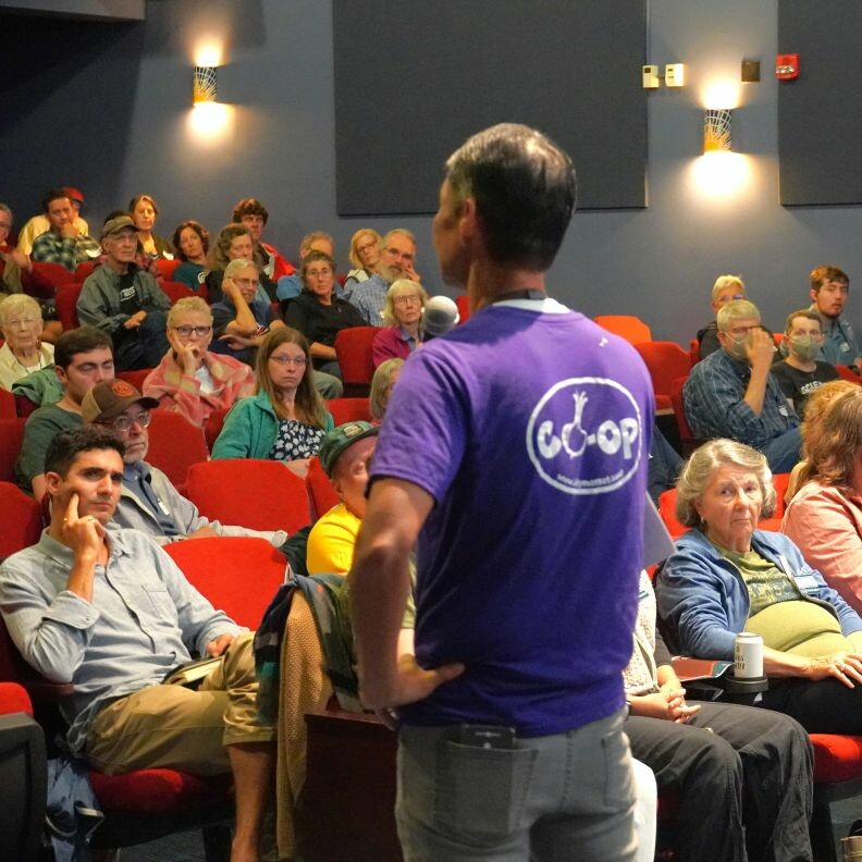 A speaker addresses an attentive audience in a theater setting.