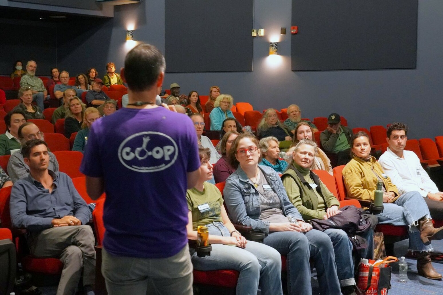 a man stands talking to a crowd in an auditorium