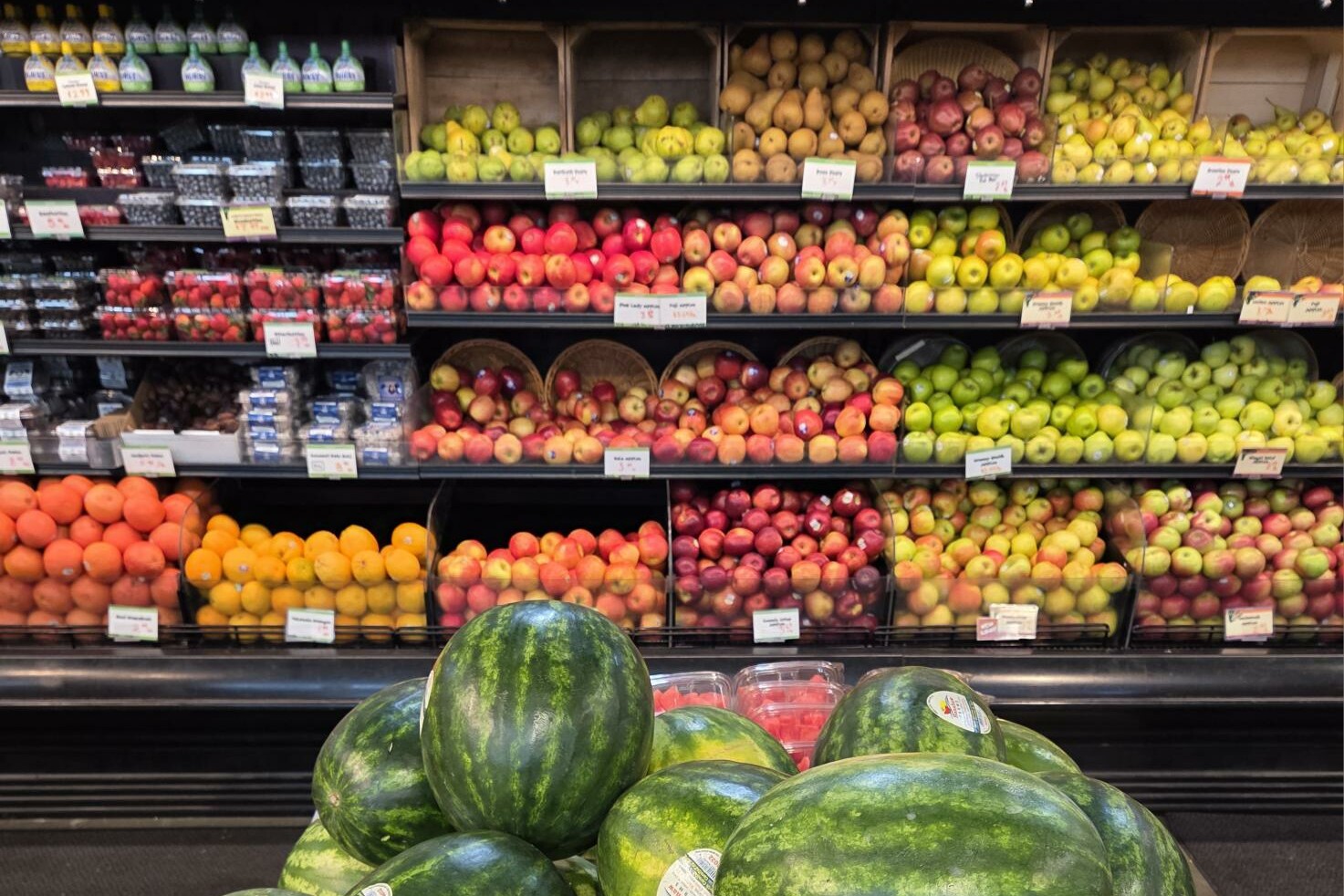 Fruit display in a grocery store featuring various apples, pears, and watermelons.