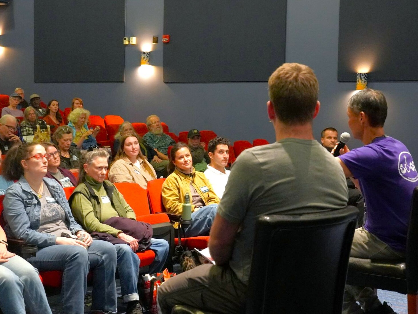 2 men sit in chairs talking with an audience in an auditorium