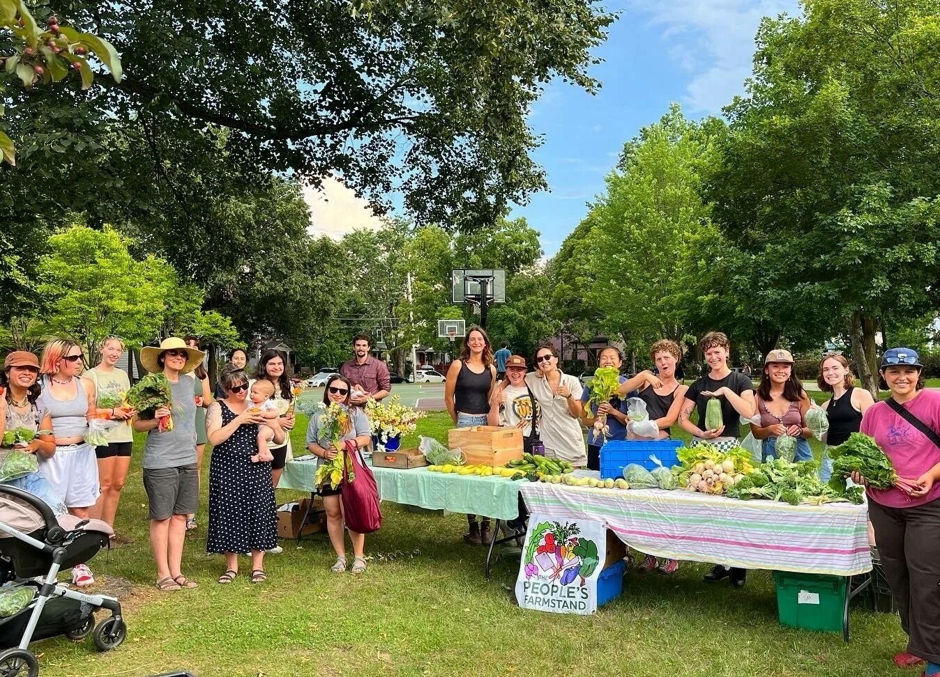 People stand outside on a summer day around a table of fresh produce