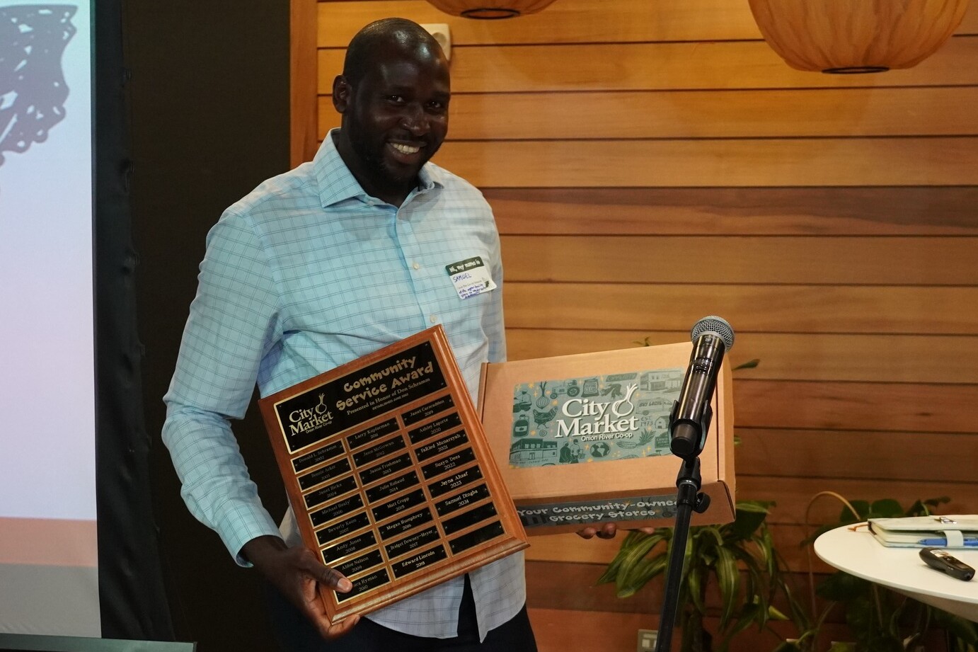 A man proudly holds a community service award and a City Market box.