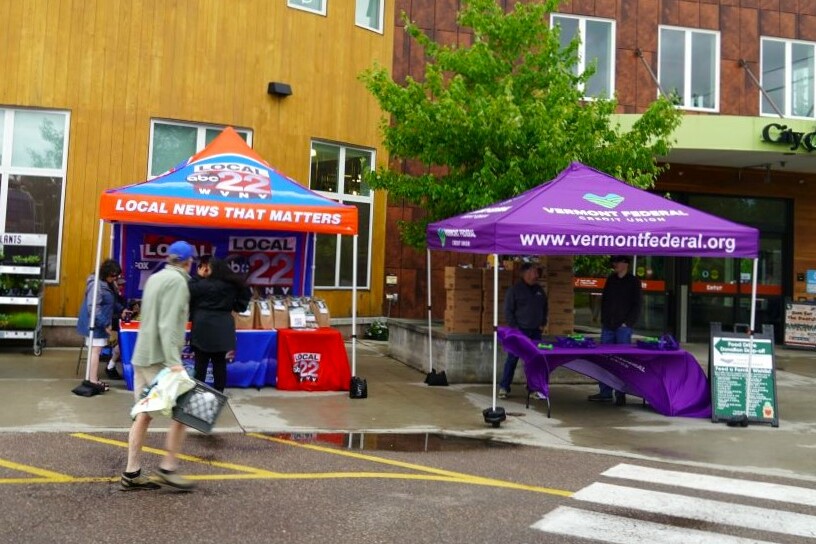 Two vendor tents outside a building, one for local news and one for a federal credit union.