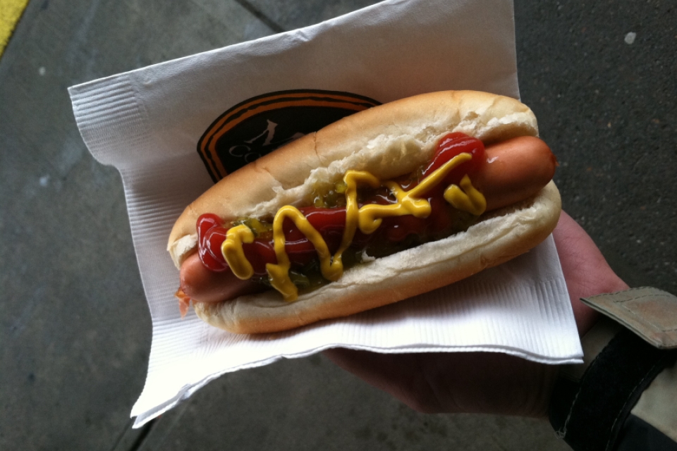 a hand holding a hot dog topped with ketchup and mustard