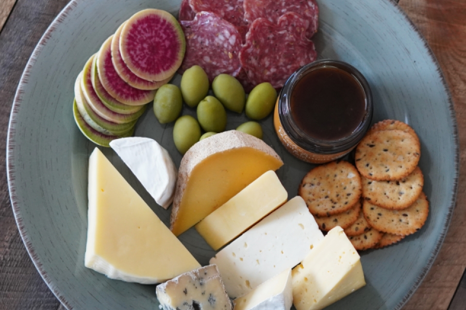 A plate of cheeses with classic cheese board accoutrements like salumi, maple fig jam, crackers, olives and daikon.