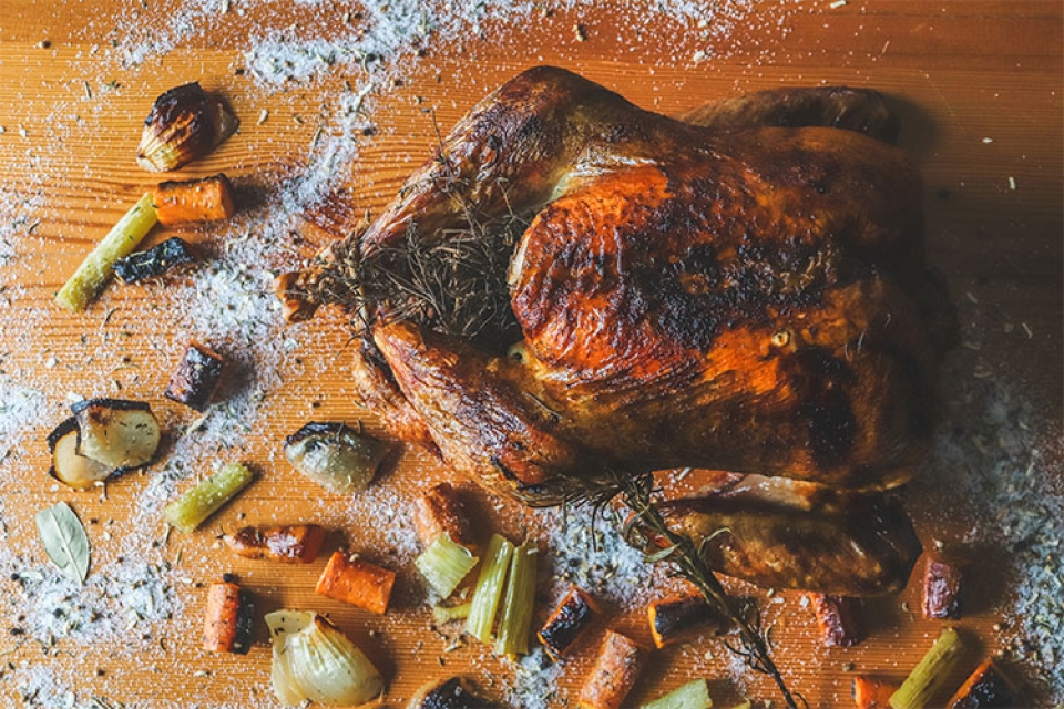 a roasted turkey on a wooden board scattered with salt and cut veggies