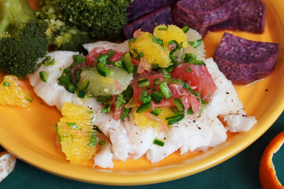 Citrus Salsa tops a white fish on a yellow plate. Beside it sit sides of purple sweet potato and broccoli