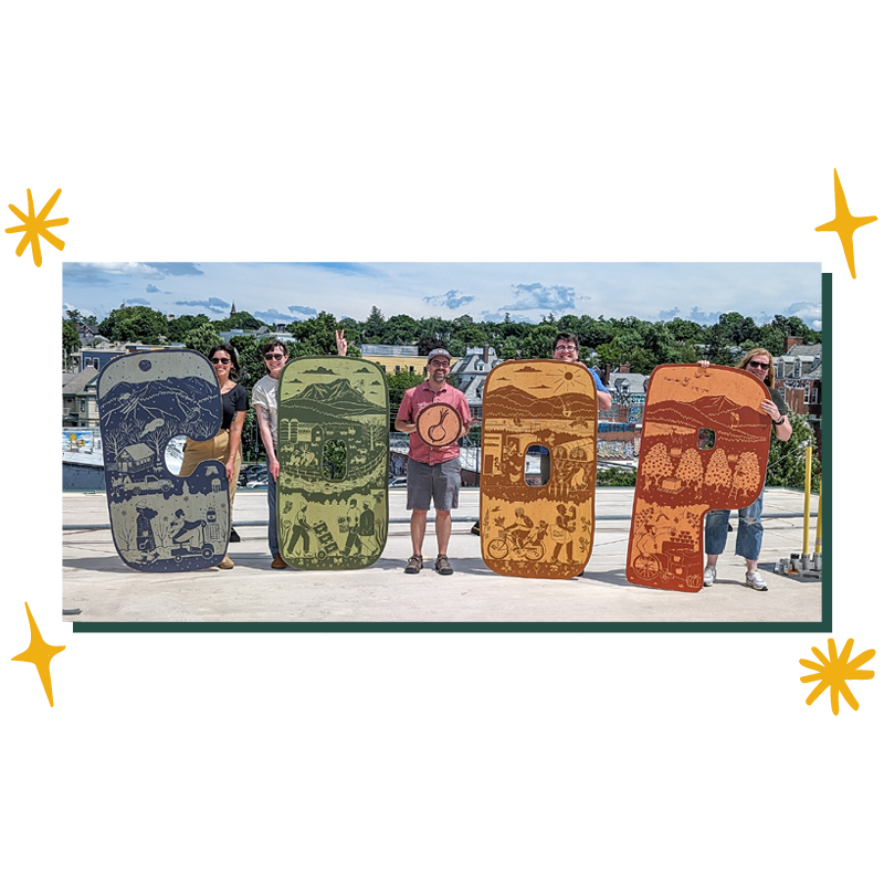 A photo of five people standing on a rooftop in bright sunlight. Four of the people hold person-sized wood cutout letters. From left to right, the letters spell "Co-op." The C is blue, the first O is green, the second O is yellow and the P is red. Each letter has illustrations on it that depict a Vermont season. Between the O's, the fifth person holds a round wood cutout with the City Market onion on it.