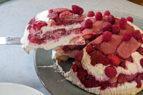 A slice of layered berry and cream cake is being lifted from the full cake.