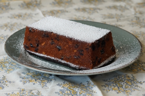 Blueberry almond loaf cake, dusted with powdered sugar, on a green plate. The plate is situated on a white and green floral tablecloth.