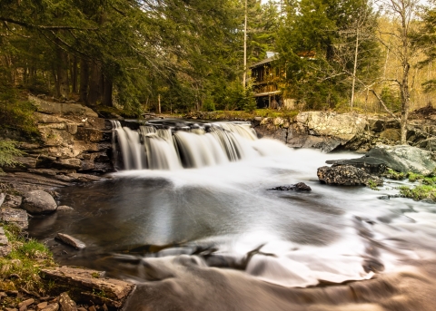 A small waterfall with white rapids. In the background are green and yellow trees and the waterfall is surrounded by rocks.