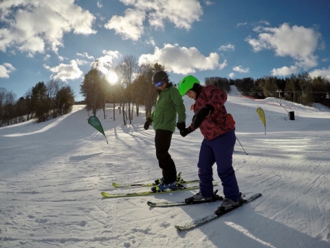 A photo of two people skiing while holding hands as the sun rises. 